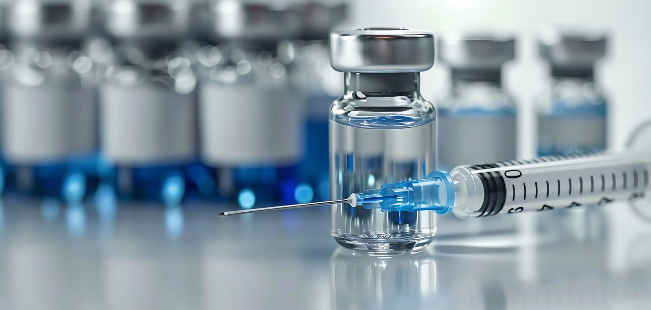 Close-up of a syringe and vaccine vial with a blue liquid, repre